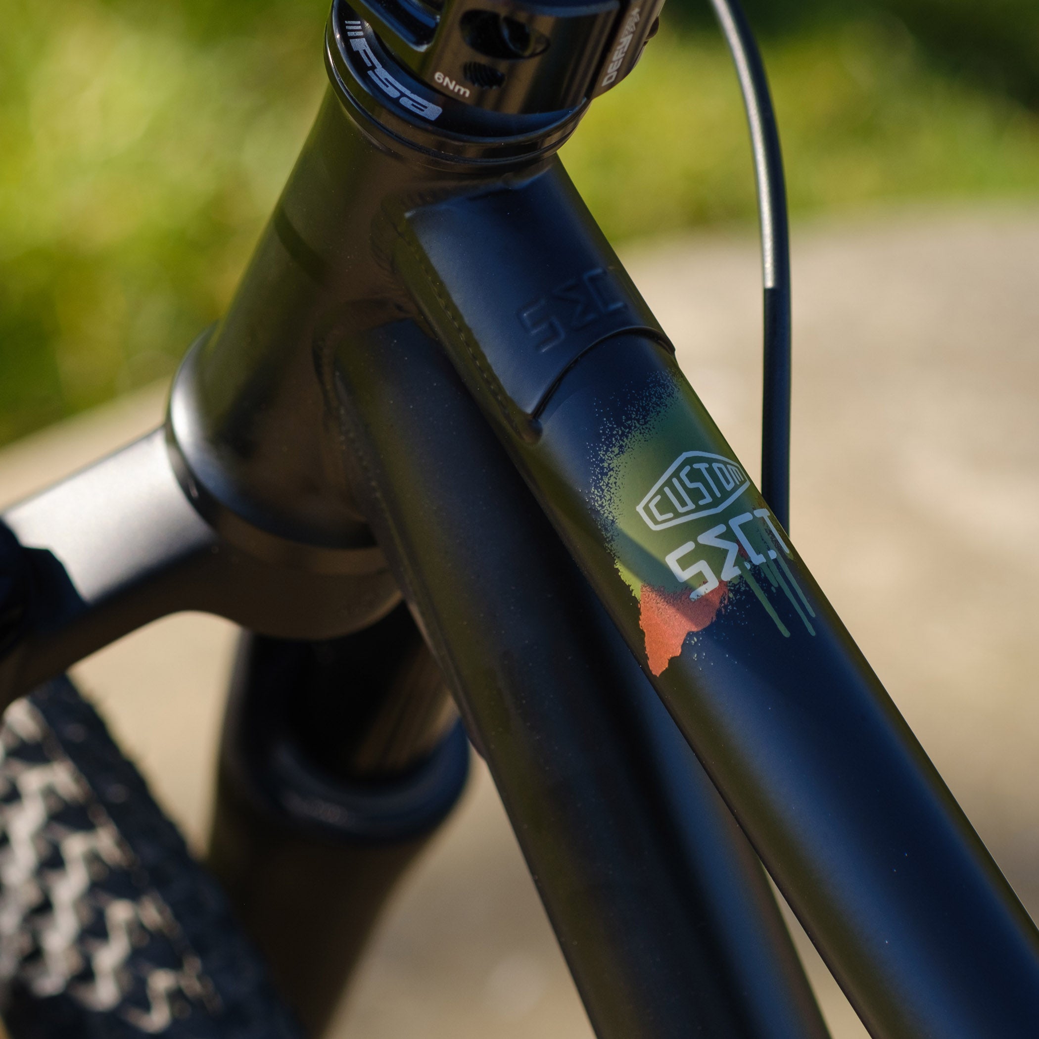 Close-up of a DMR Sect Custom 24" off-road mountain cycling cycle bike bicycle frame's top tube, in matt black, with visible branding. A blurred brown background can be seen.