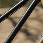 Close-up of a DMR Sect Custom 24" off-road mountain cycling cycle bike bicycle frame's down tube, in matt black, with visible branding. A blurred brown background can be seen.