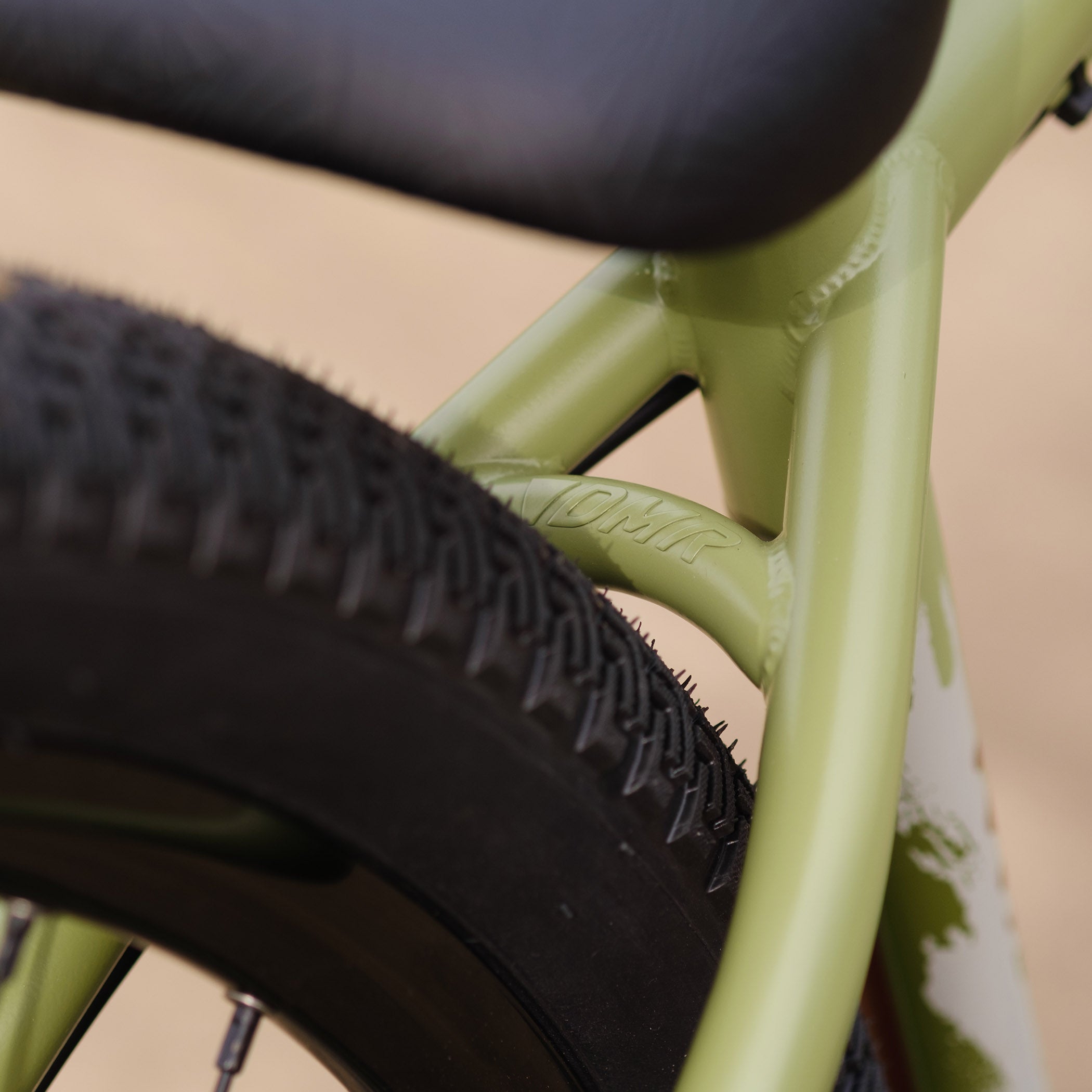 Close-up of a DMR Sect Custom 26" off-road mountain cycling cycle bike bicycle frame's seat stays, in pistachio green, with visible branding. A blurred brown background can be seen.