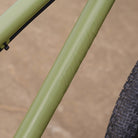 Close-up of a DMR Sect Custom 26" off-road mountain cycling cycle bike bicycle frame's down tube, in pistachio green, with visible branding. A blurred brown background can be seen.