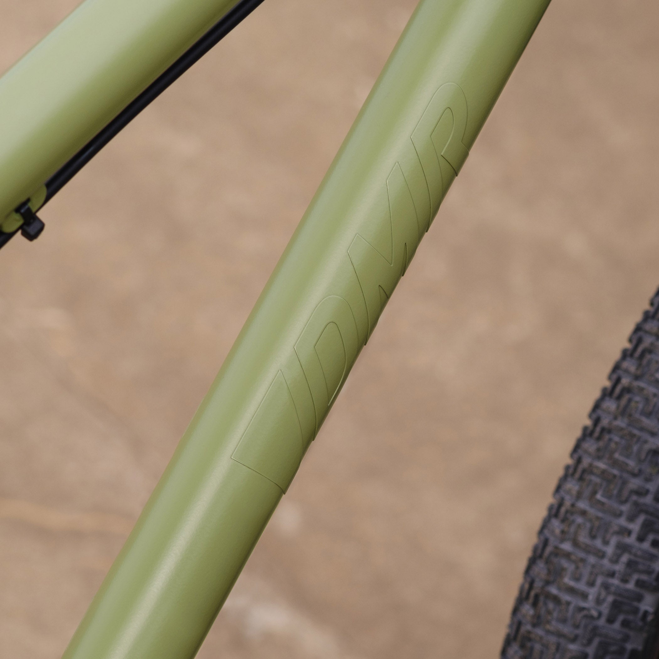 Close-up of a DMR Sect Custom 26" off-road mountain cycling cycle bike bicycle frame's down tube, in pistachio green, with visible branding. A blurred brown background can be seen.