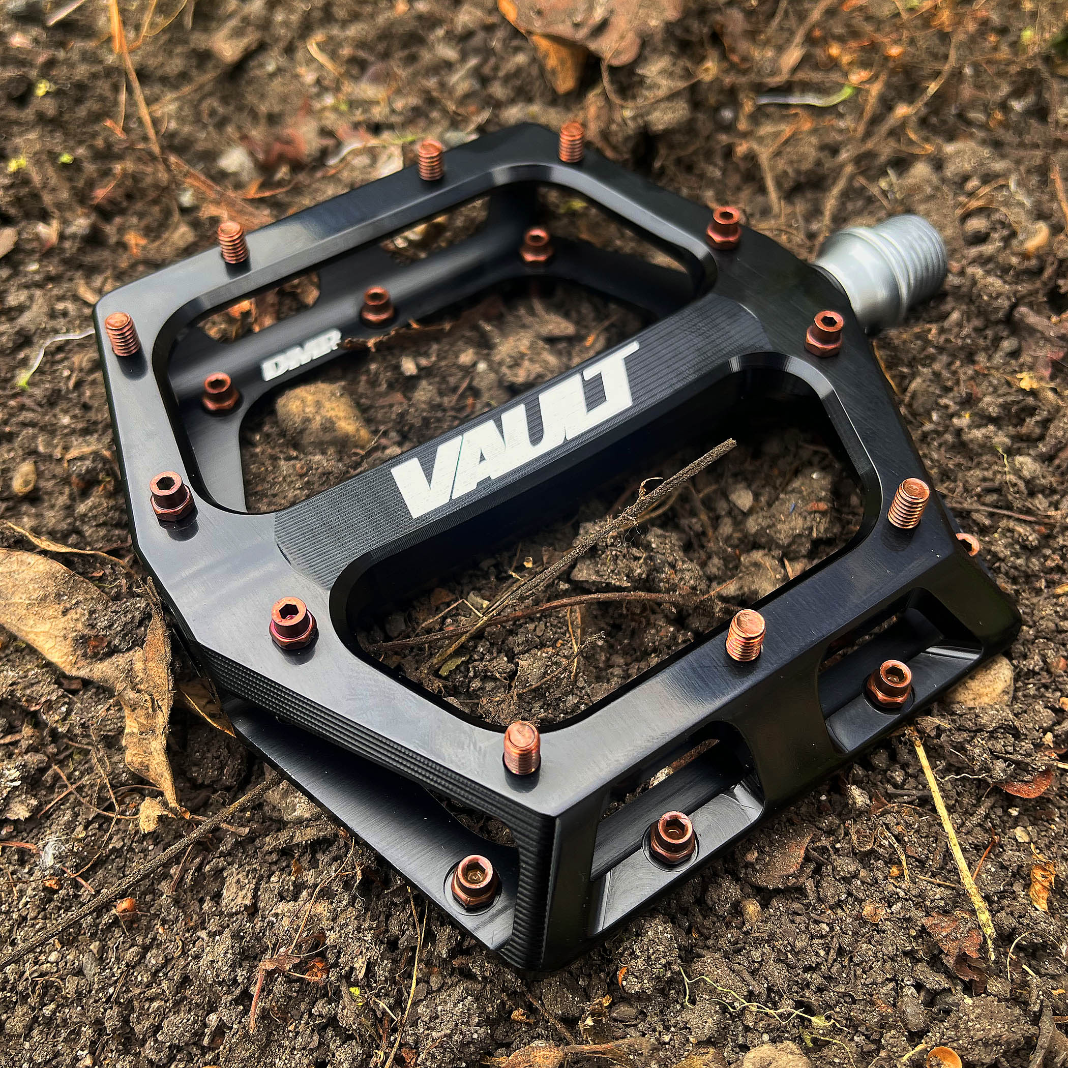 Black DMR Vault with copper bronze brown coloured pins, placed upon dirt. The dirt is brown.