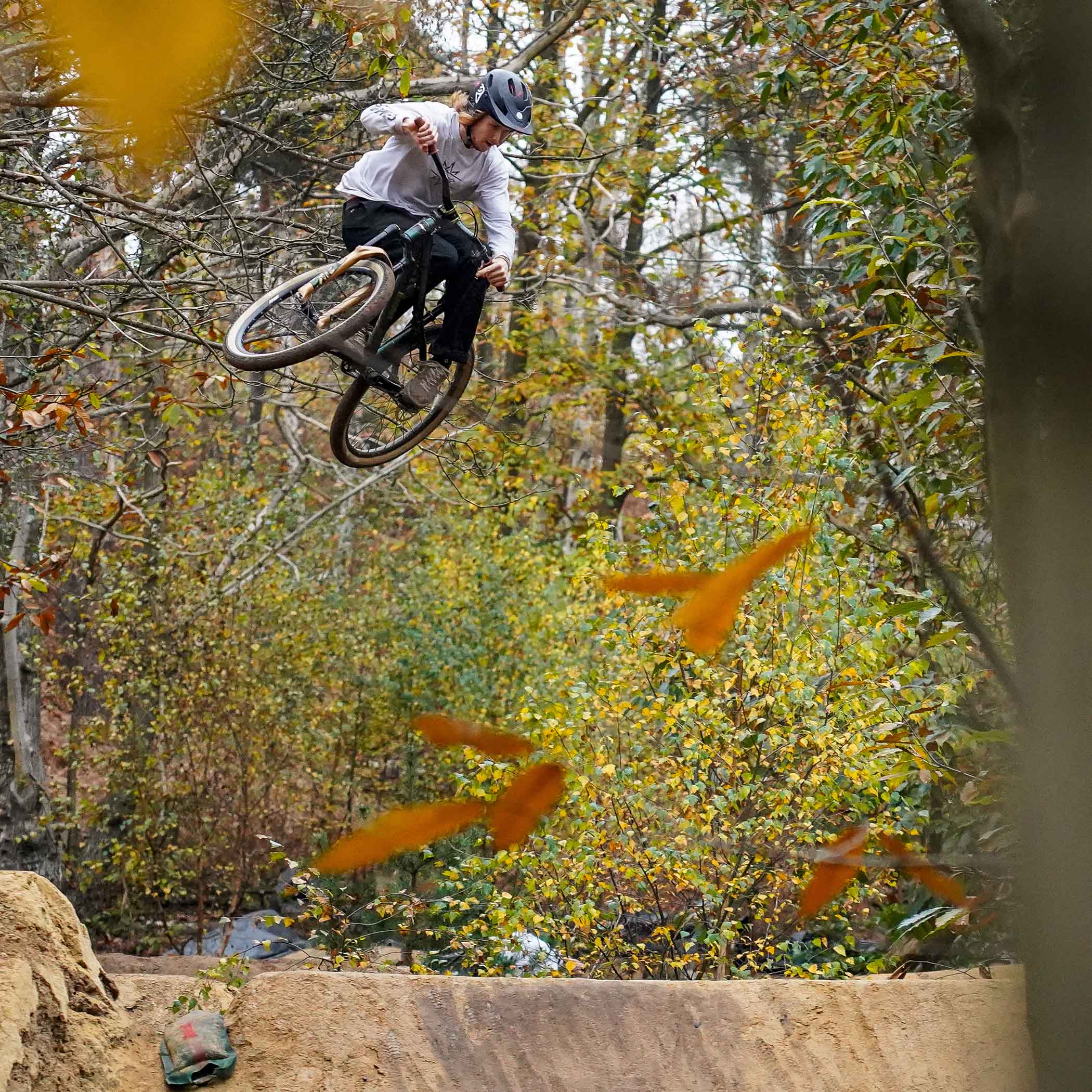 A person with a name of Andy Lehmann, riding on a DMR Rhythm off-road mountain cycling bicycle bike, performing an aeronautical manoeuvre in a forest with autumn leaves.