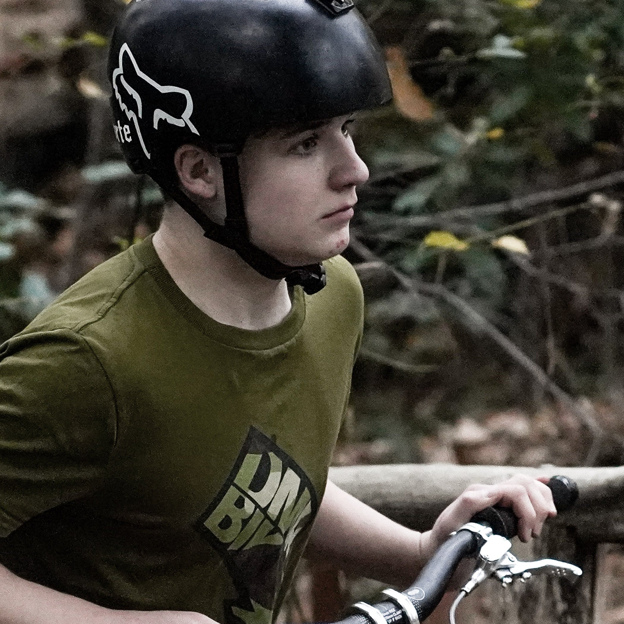 Person wearing a helmet and green t-shirt with a logo, sitting outdoors.