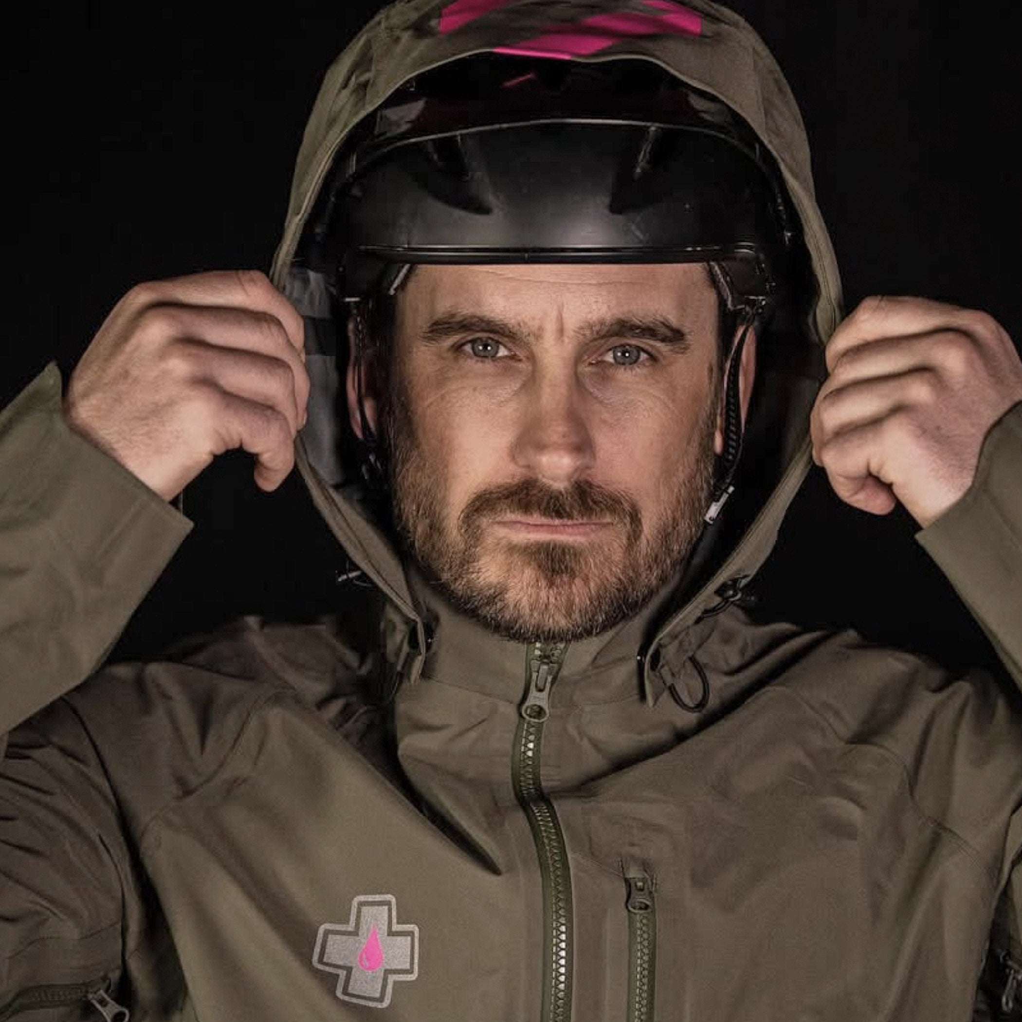 Man wearing a brown jacket with a hood and a helmet, against a black background