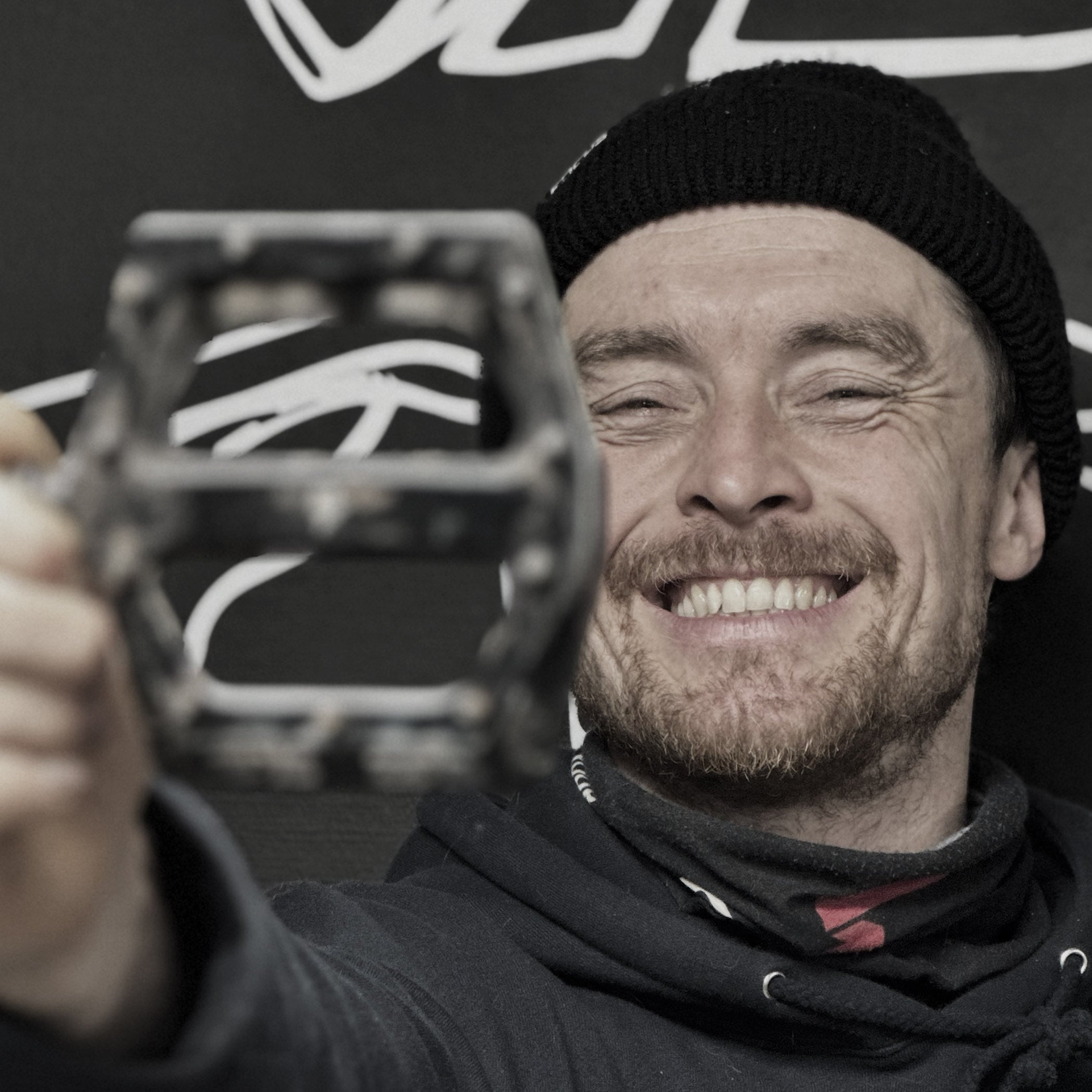 Man holding a bicycle pedal with a brand logo in the background