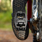 Black DMR VMAX off-road mountain cycle cycling pedal pedalling product, under the foot of a rider, with a blurry green background.