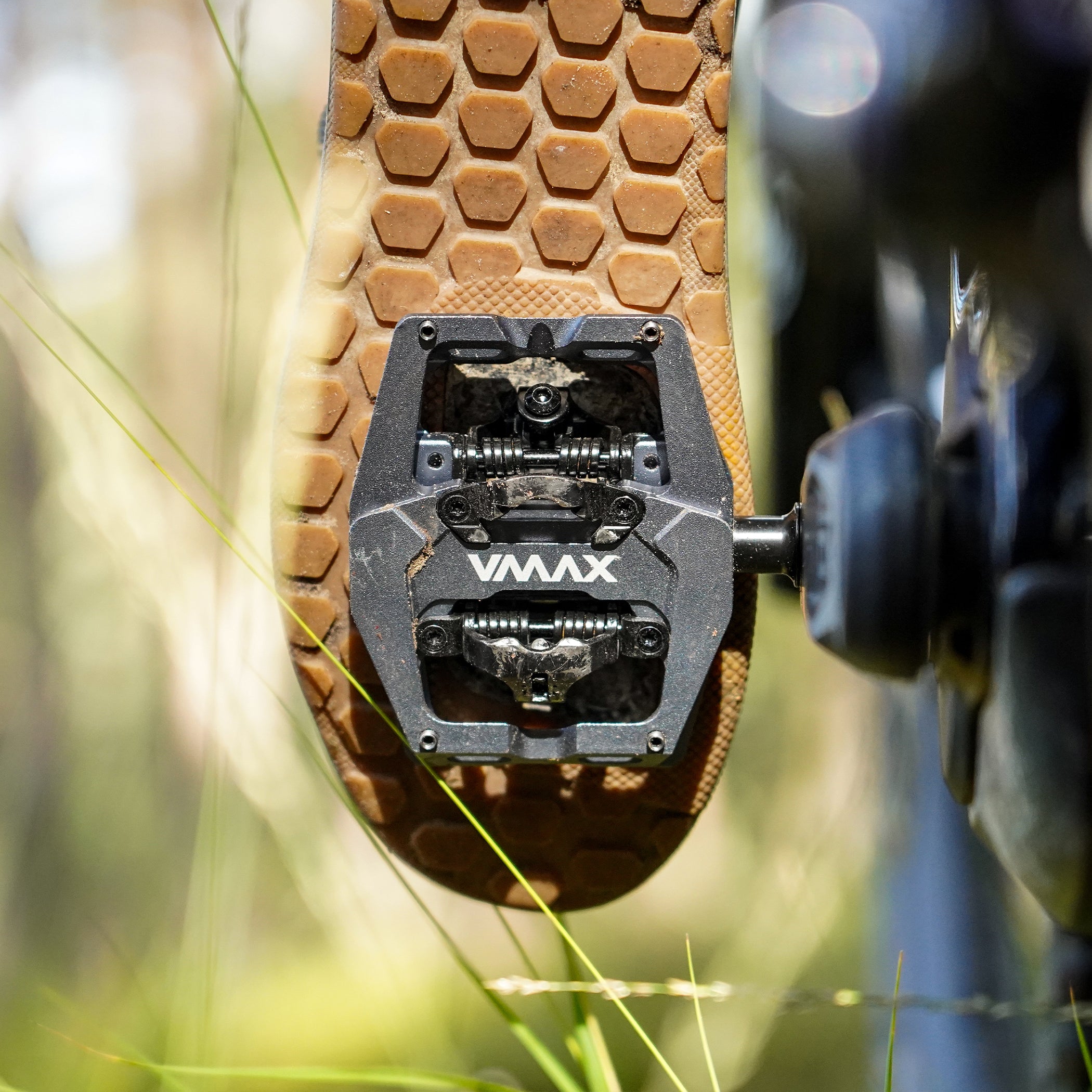 Grey DMR VMAX off-road mountain cycle cycling pedal pedalling product, under the foot of a rider, with a blurry green background.