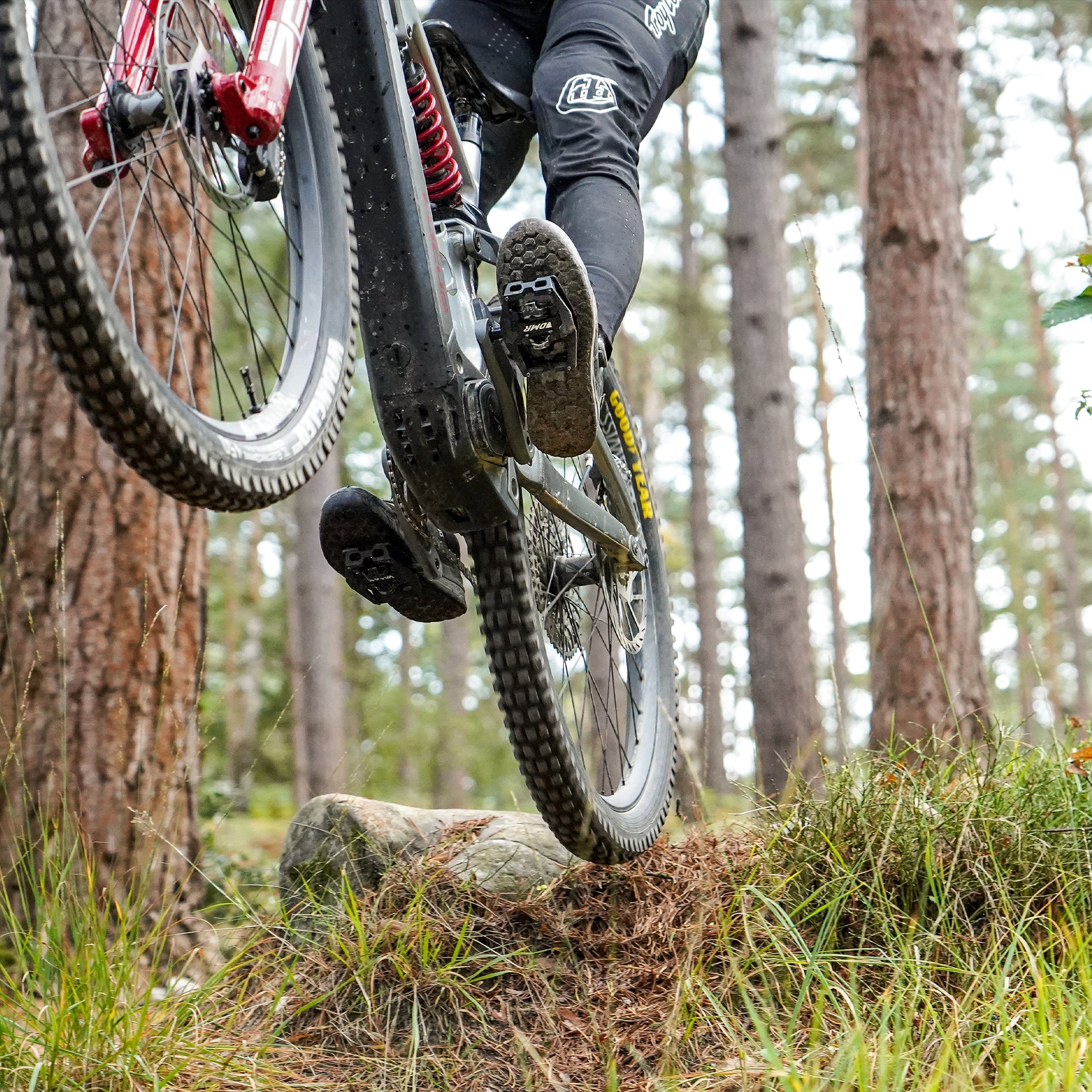 Black DMR VMAX off-road mountain cycle cycling pedal pedalling product, under the foot of a rider, with a blurry green background.