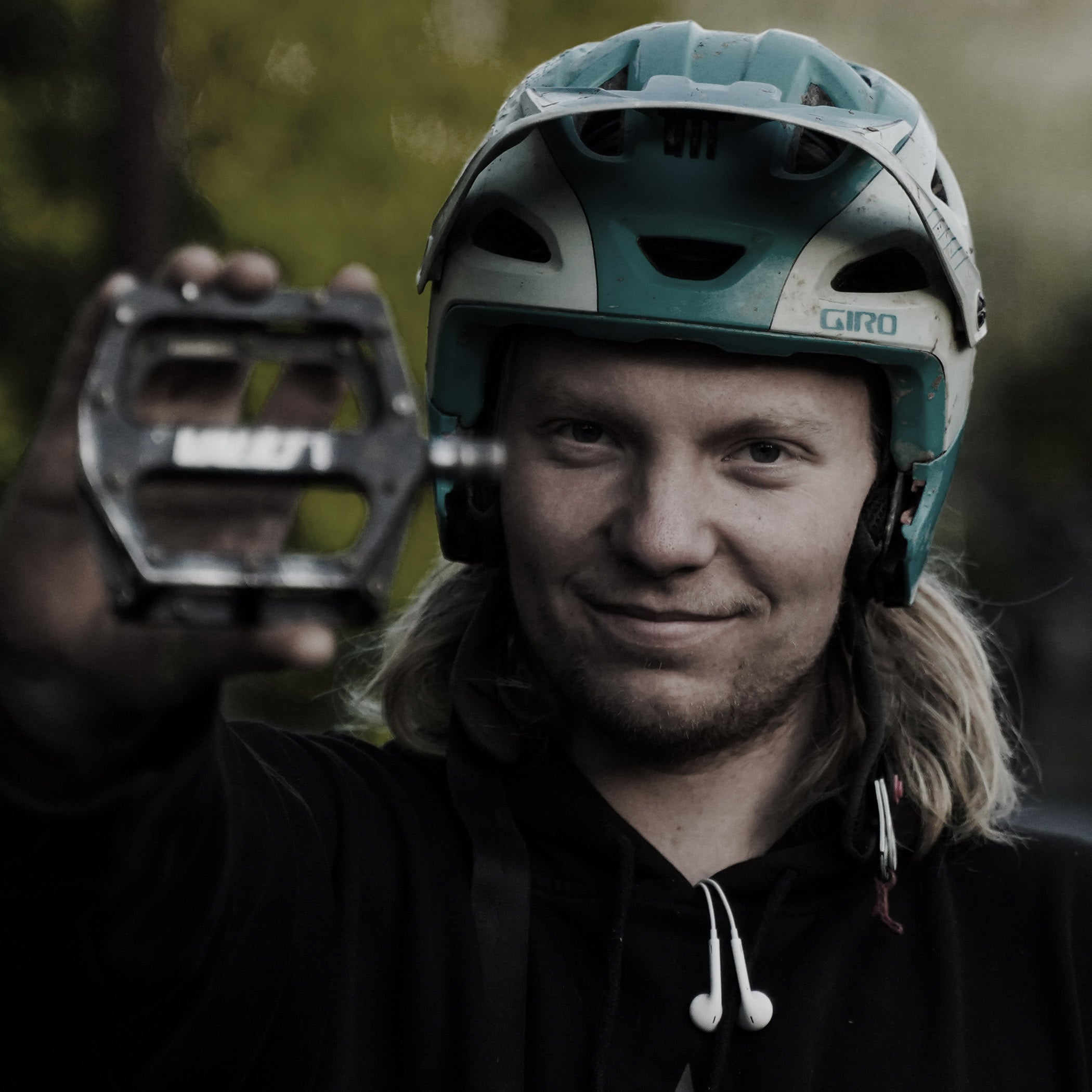 Person wearing a helmet holding a bicycle pedal with a blurred natural background