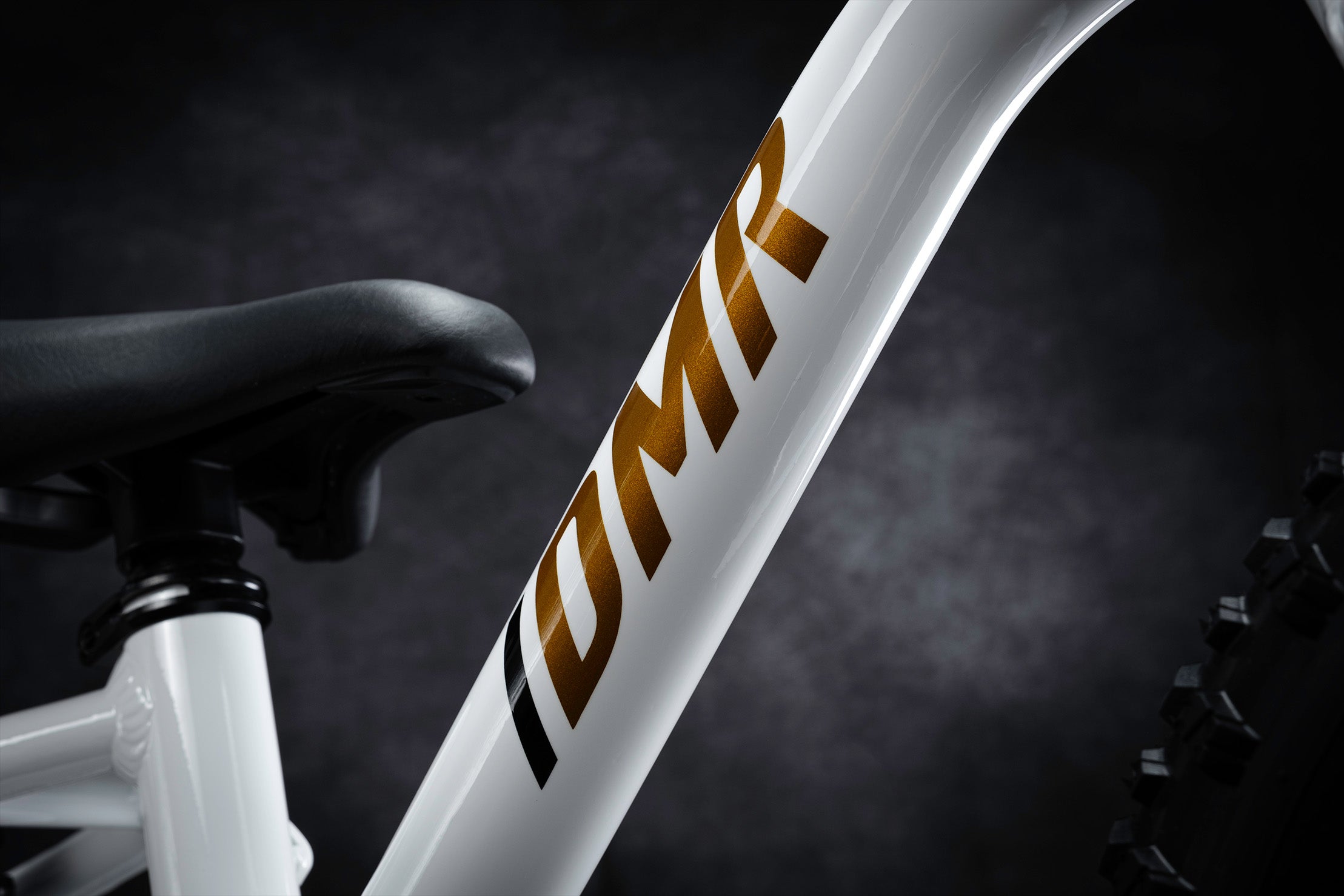 a close-up of the dmr sidekick balance bicycle kids childrens bike for cycling, featuring a dmr bicycles and dirt logo placed upon the downtube of the bike bicycle for kids. This dmr bicycles and dirt logo is a metallic bronze colour, with a black stroke line beforehand.