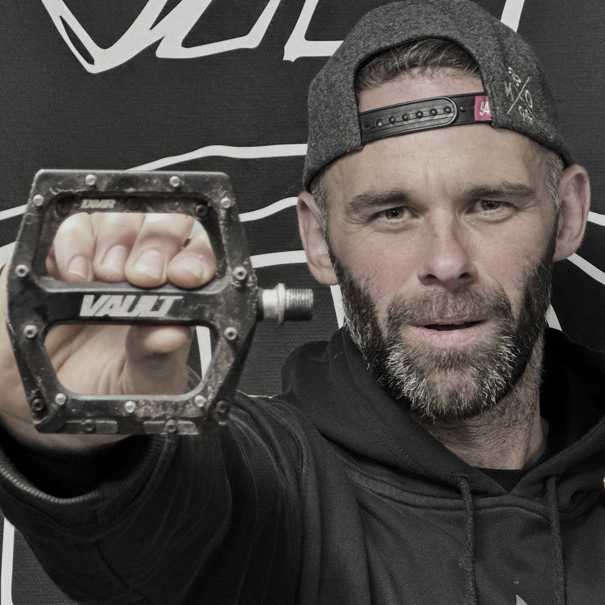 Man holding a black pedal with 'Vault' branding against a black background with white text.