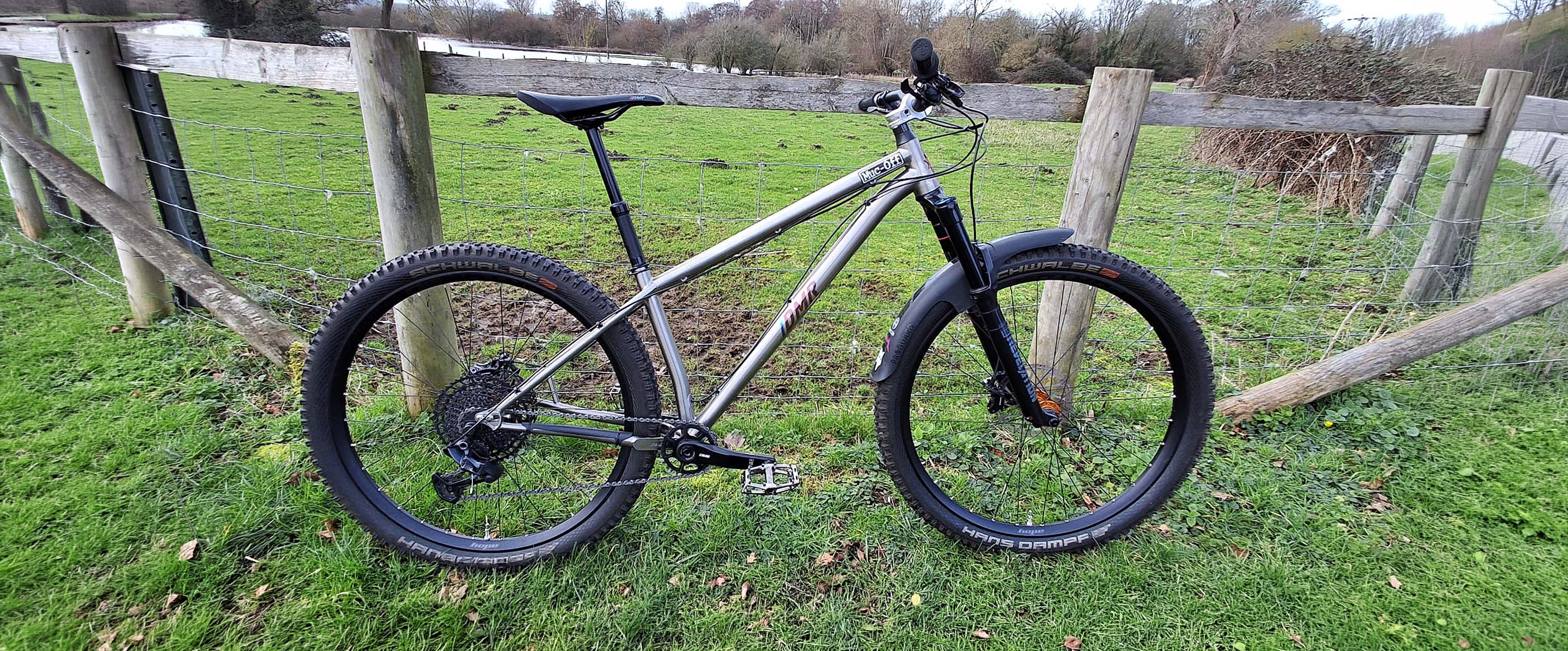 DMR Trailstar Titanium Bicycle parked on grass next to a wooden fence