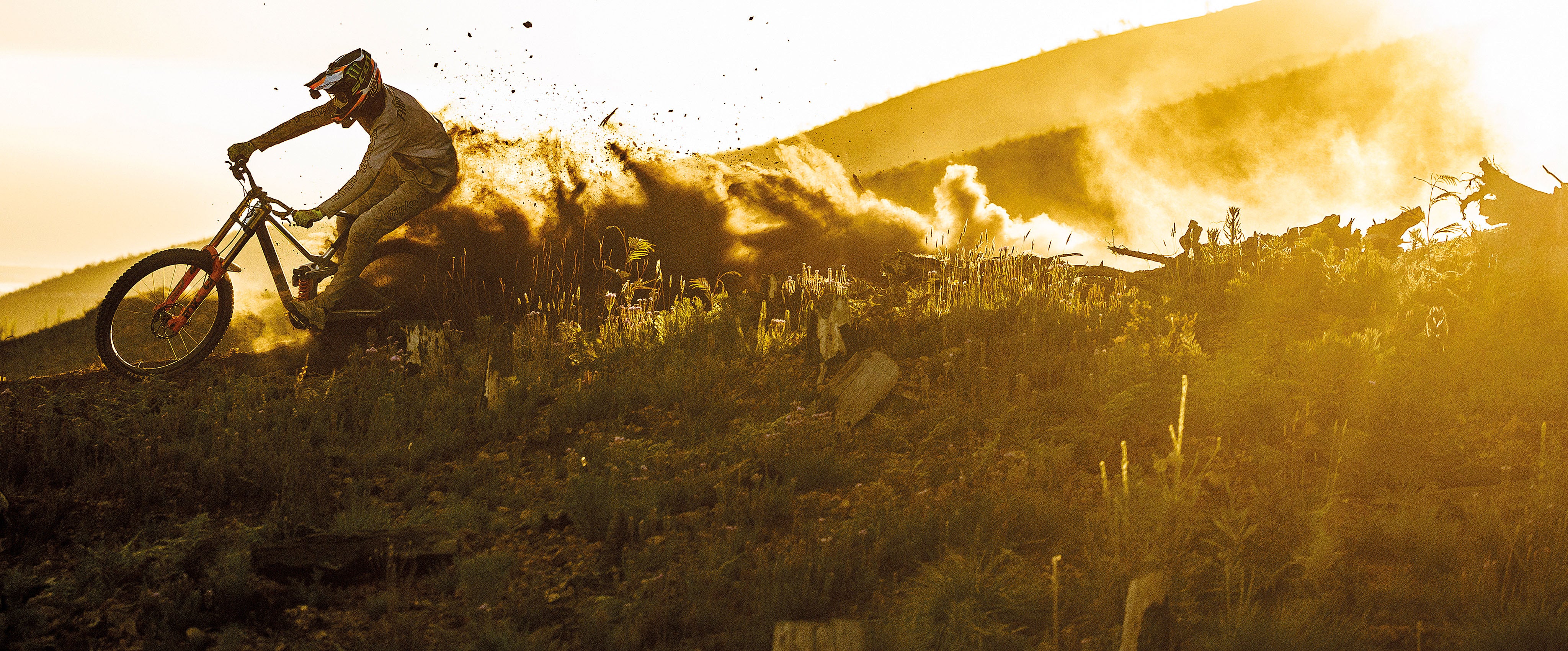 Person riding a bicycle on a grassy hill with a golden sunset