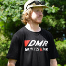 Team rider Andy Lehmann wearing a black t-shirt with DMR Bicycles & Dirt logo standing against trees in the ackground