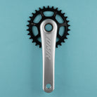 A DMR crank arm and black chainring set against a solid light blue background.