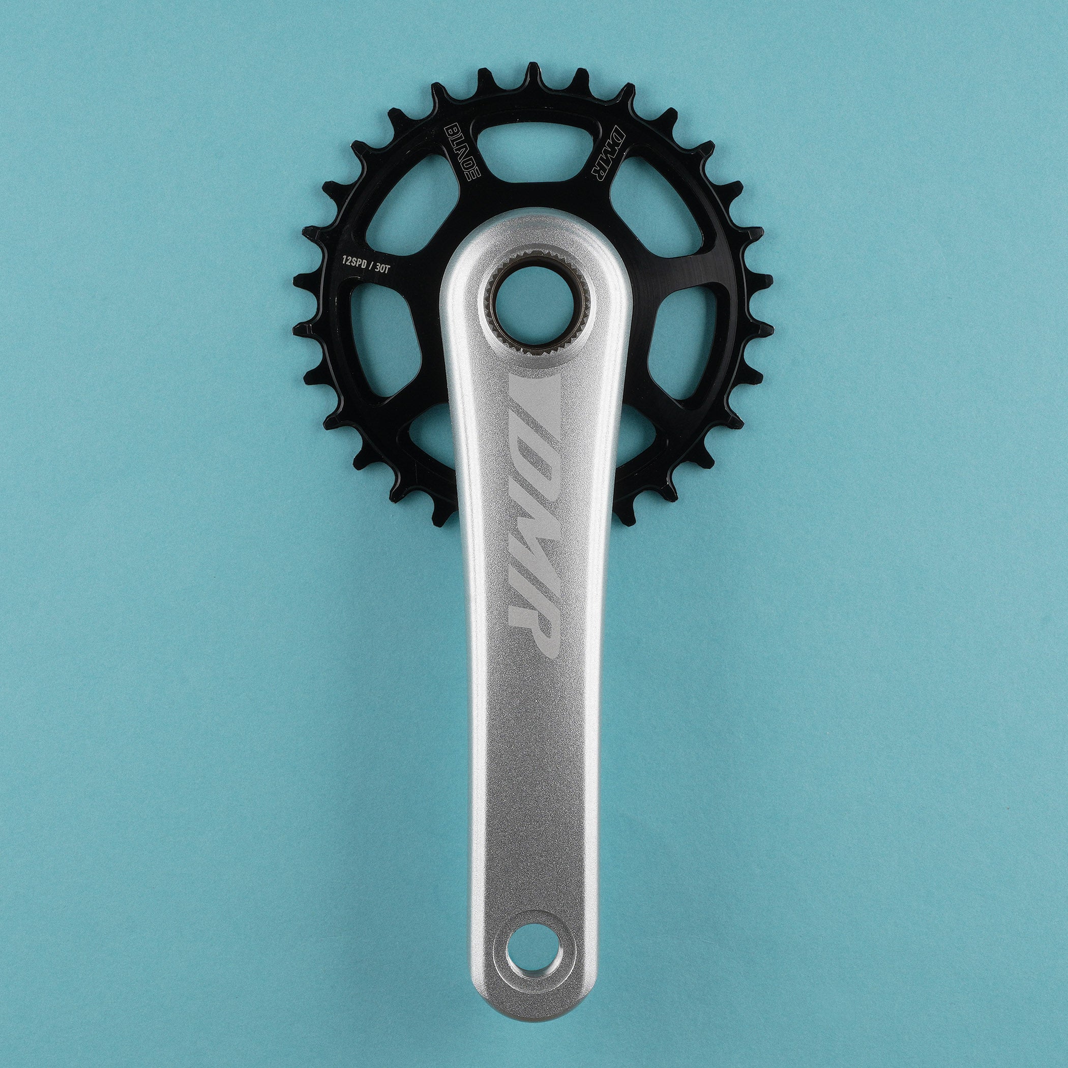 A DMR crank arm and black chainring set against a solid light blue background.