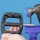 silver dmr bikes bicycles vmax vault mag magnesium midi v12 v11 flat4 flat 4 four versa clip clipless pedals pedal service servicing tool in use with allen key and hammer in a vice on a blue background