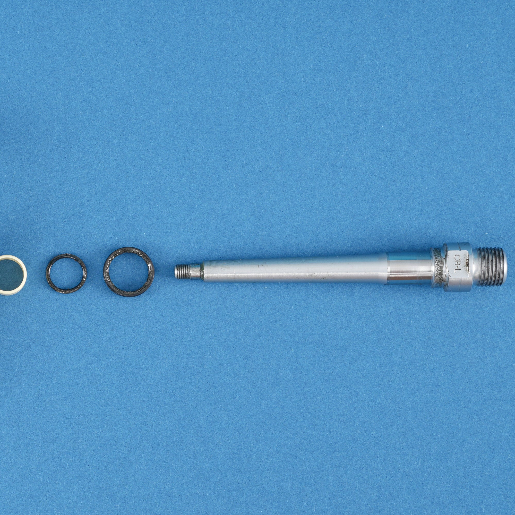 silver pedal axle with bushing and seals arranged on a blue background