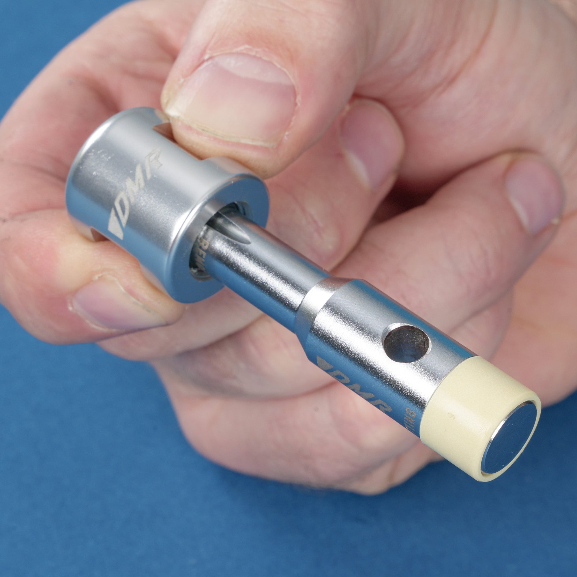 a close-up of a hand holding the silver dmr bikes bicycles vmax vault mag midi v12 v11 flat4 flat 4 four versa clip clipless pedals pedal service servicing tool with bushing fitted on a blue background