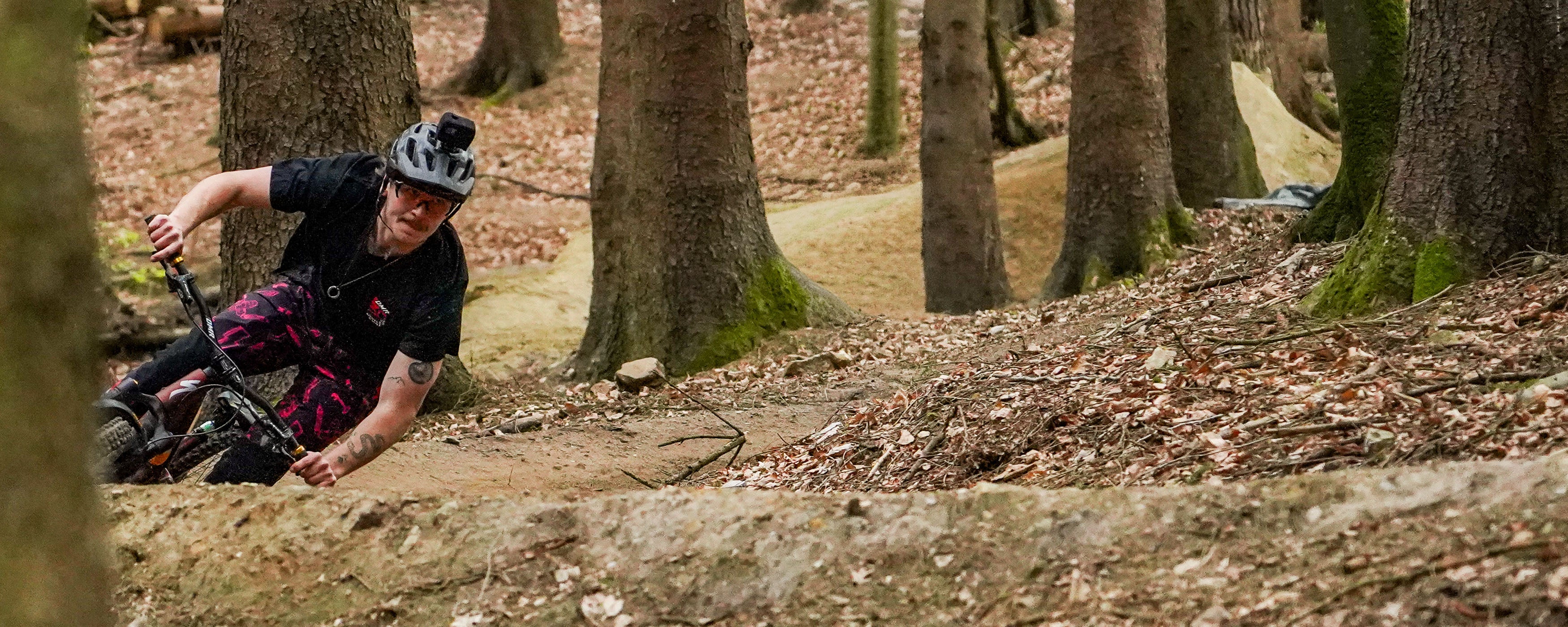 DMR team rider, Preston Williams mountain biking through a forest trail with trees and fallen leaves.