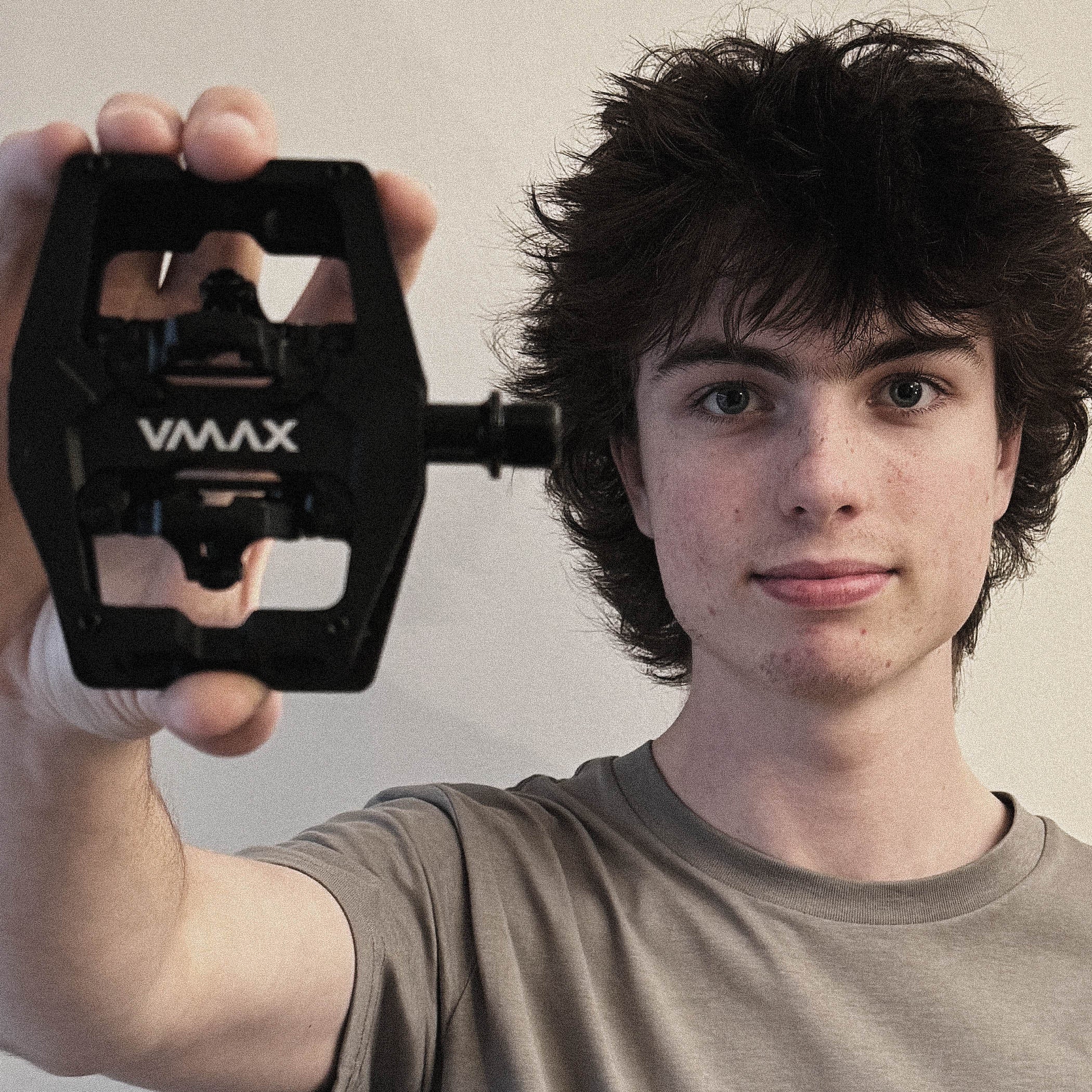 Person holding a black VMAX bike pedal against a plain background