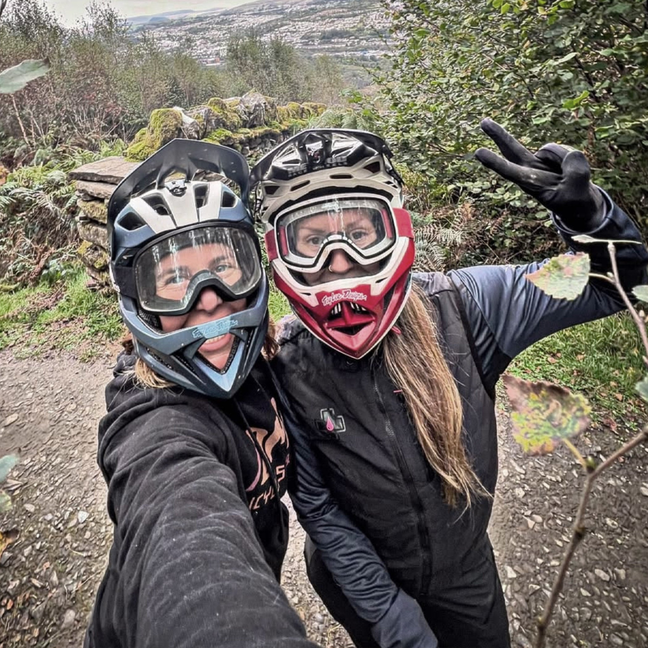 Two people wearing helmets and goggles outdoors on a trail.