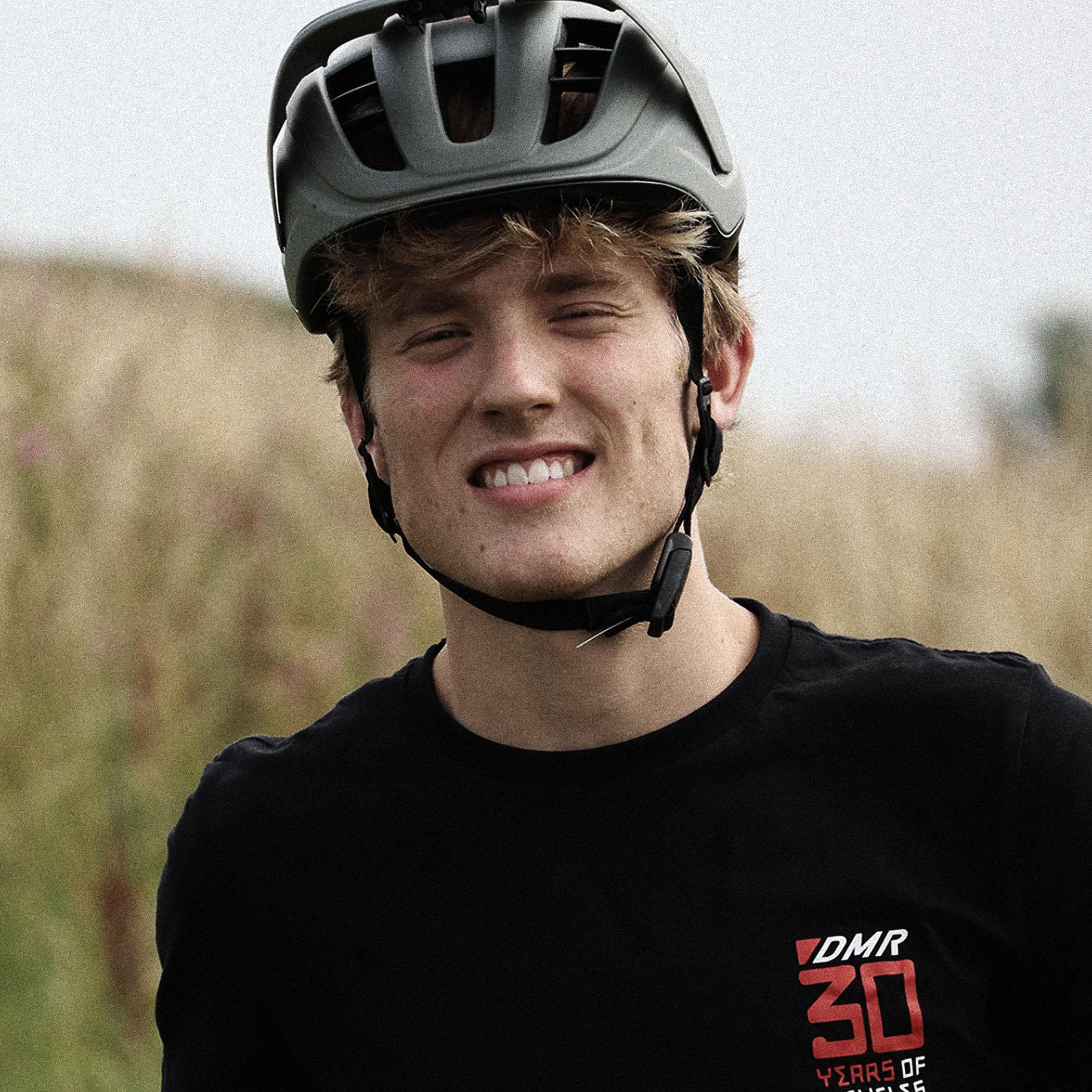 Person wearing a bicycle helmet and black shirt with DMR logo in an outdoor setting