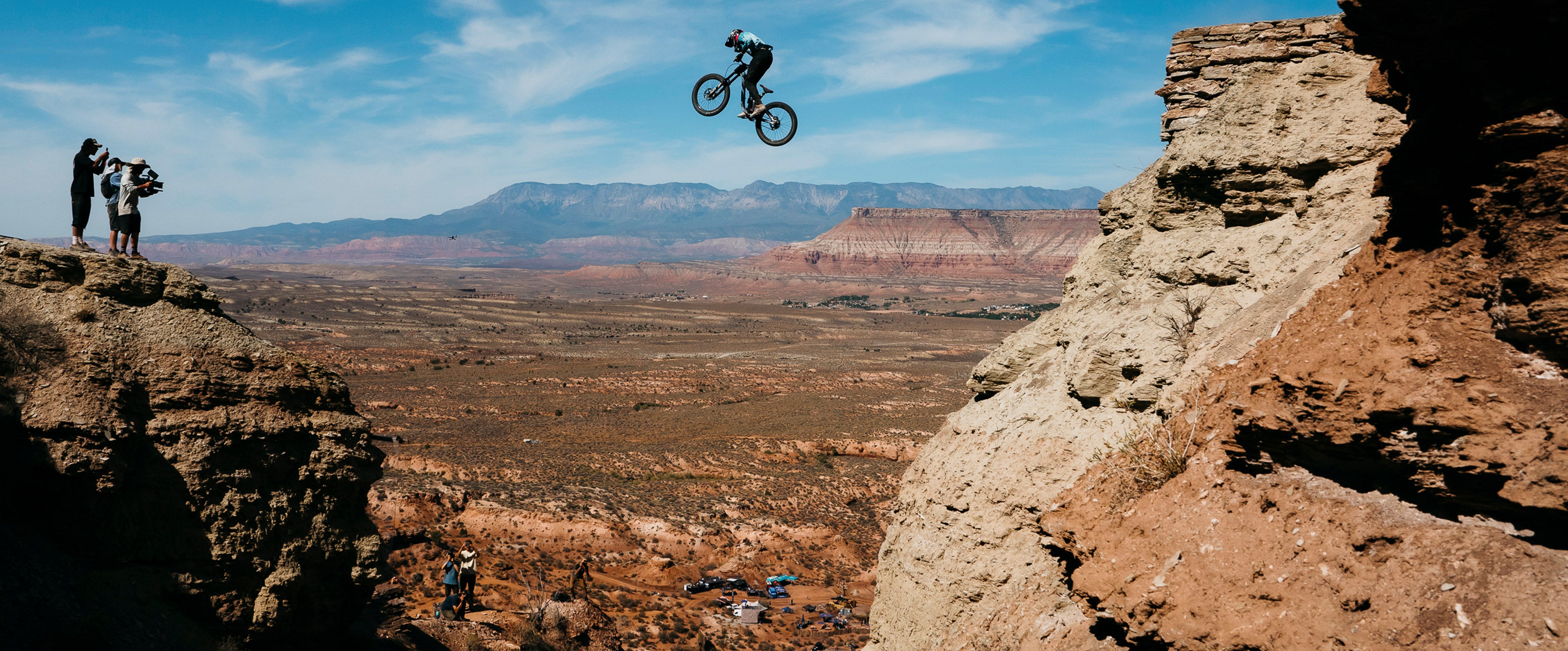 Person on a bike performing a jump over a canyon with mountains in the background