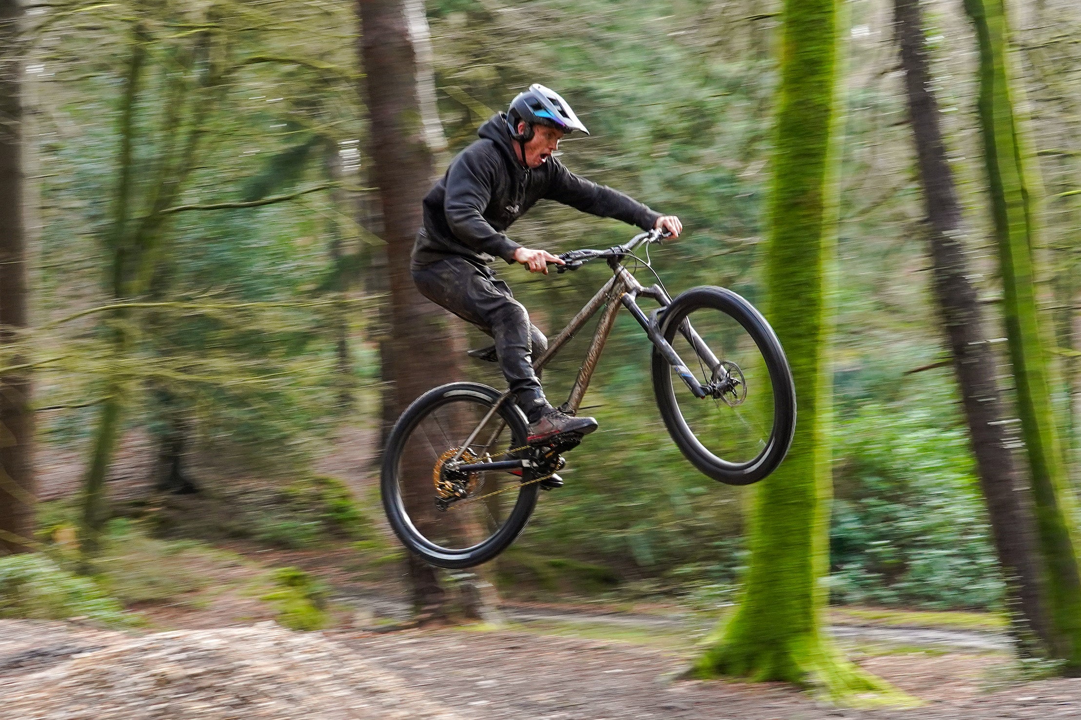 DMR Trailstar Ti Frame, built into a Mountain Bike, being ridden by a man called "Sam Marzetti" over a jump in the woods.