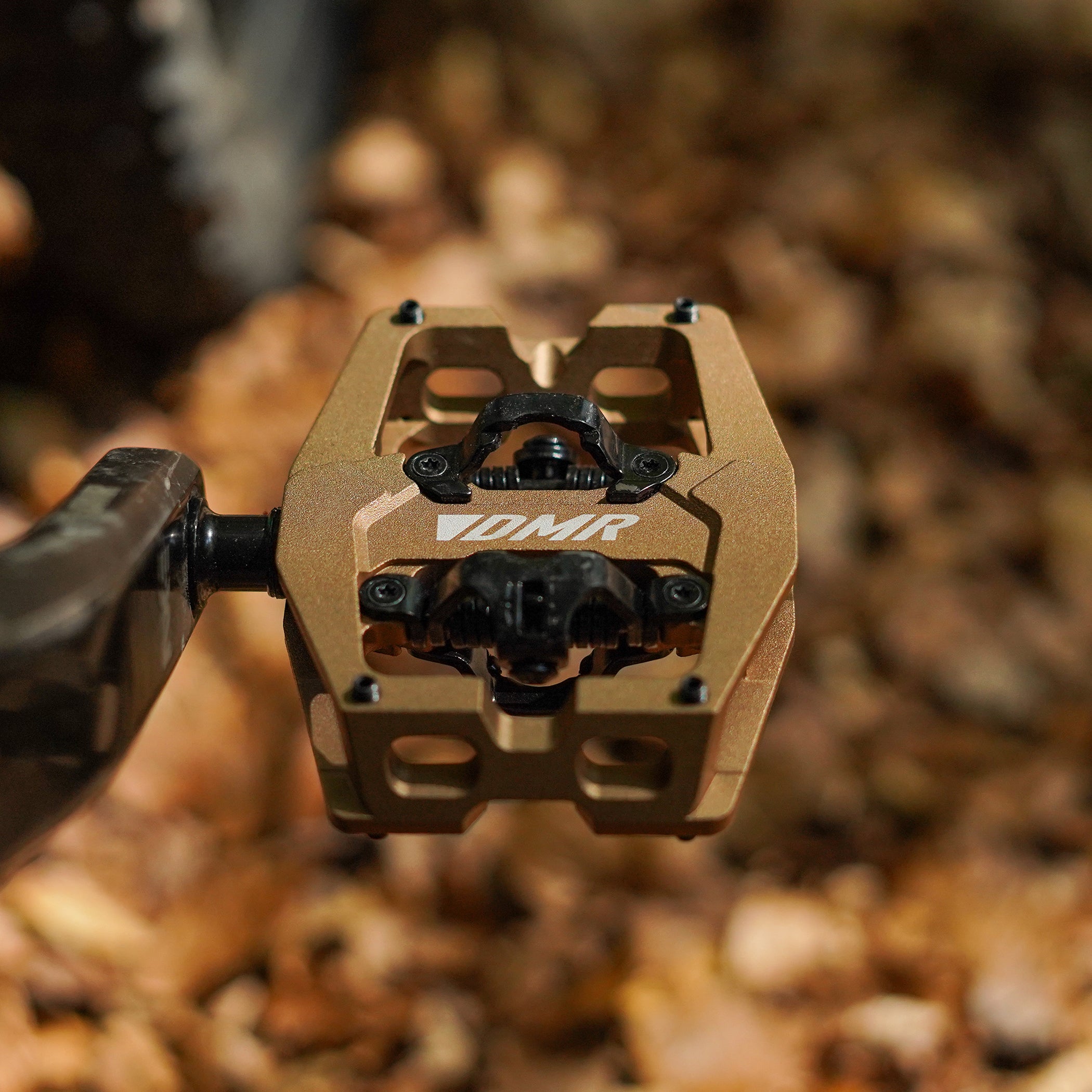 Close-up of the Light Bronze DMR VMAX clipless clip-in clip clipped SPD off-road mountain cycling bicycle bike pedalling pedal product, with an autumnal background composing of leaves other foliage.