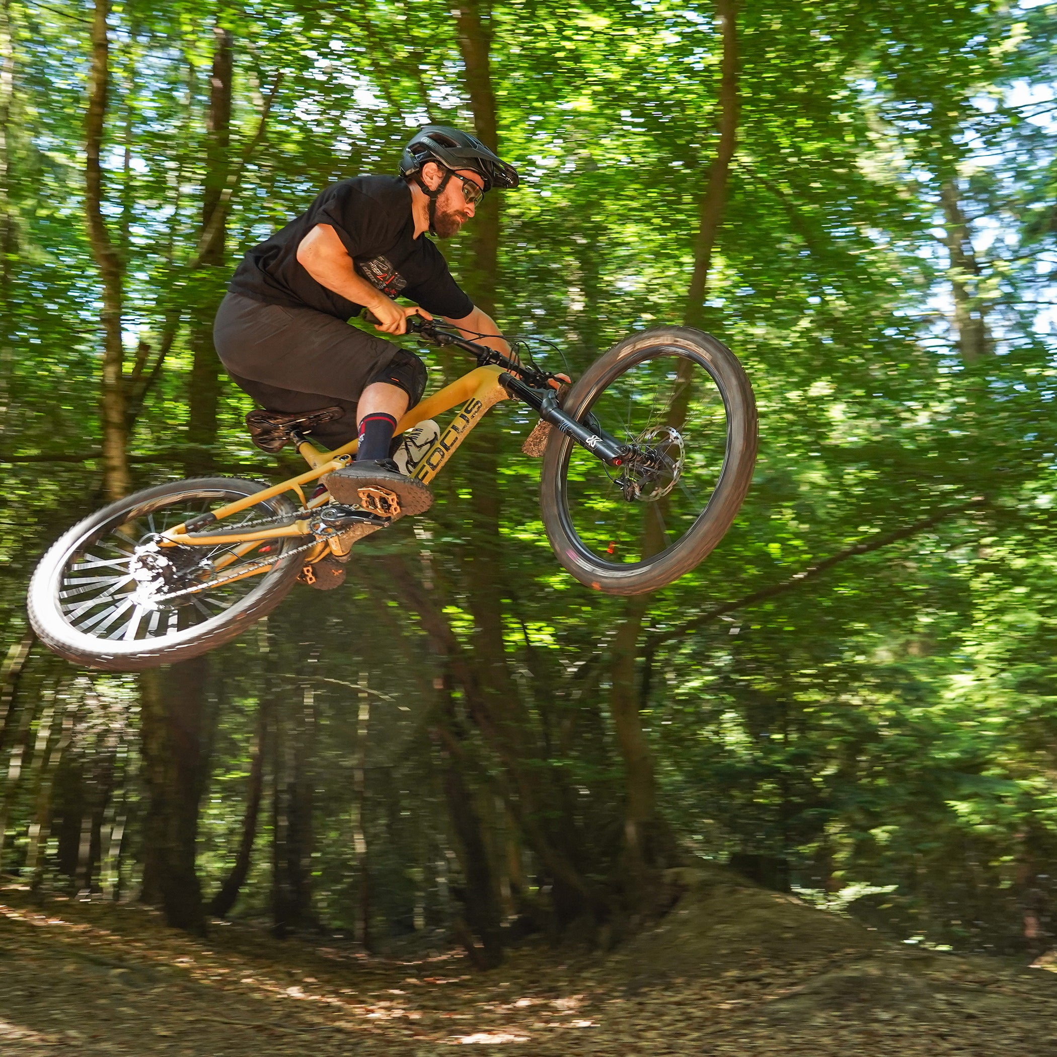 Light Bronze DMR VMAX clipless clip-in clip clipped SPD off-road mountain cycling bicycle bike pedalling pedal product, being used on an off-road mountain cycling cycle bicycle bike, pictured riding off a jump in the woods.