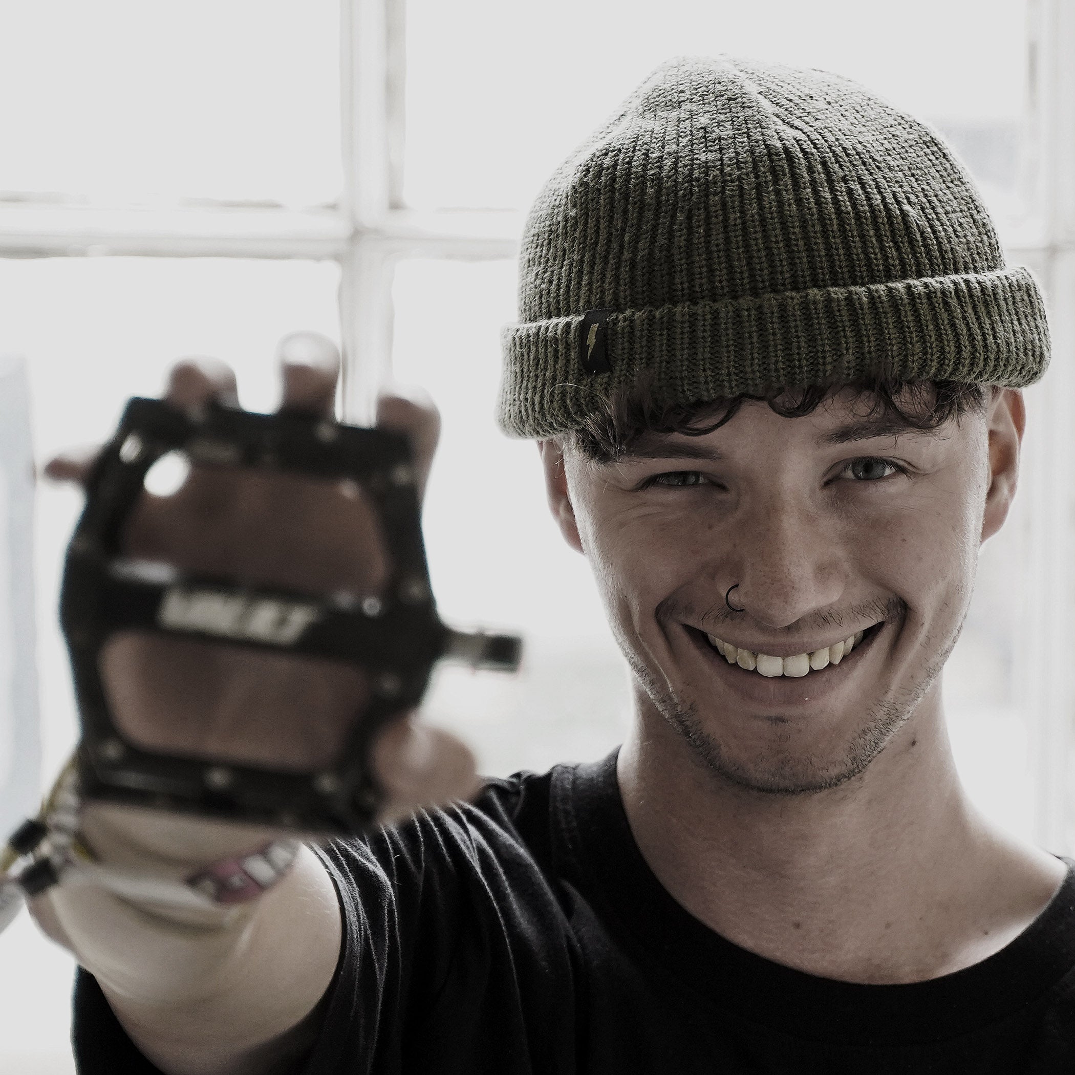 Person wearing a green beanie and black gloves, holding up a glove with a brand logo.