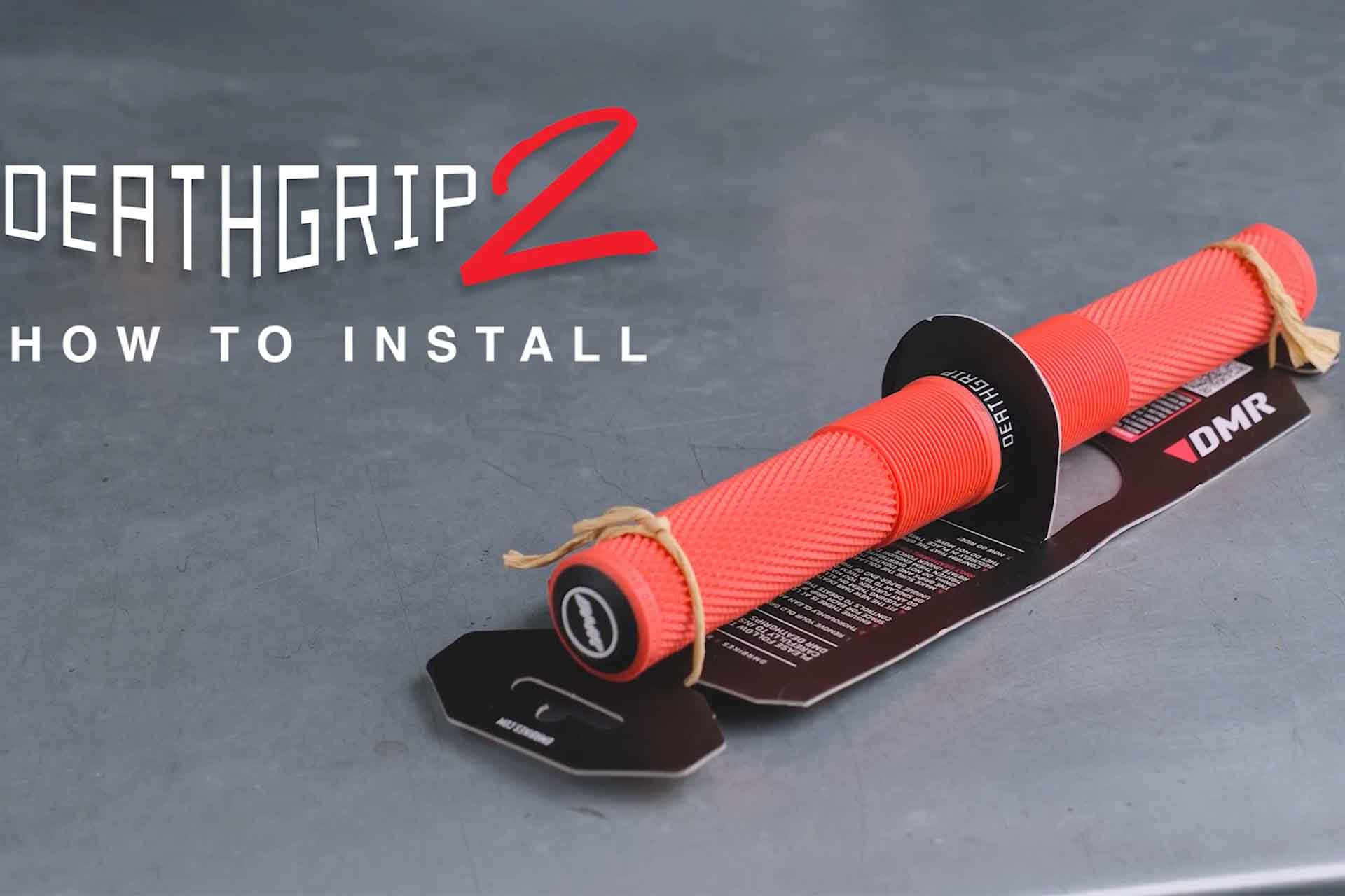 DMR Deathgrip2 off-road mountain cycling hand holding grip items, place upon a metal table top. These DMR Deathgrip2 off-road mountain cycling hand holding grip items are Red in colour. White title text on the left hand side.