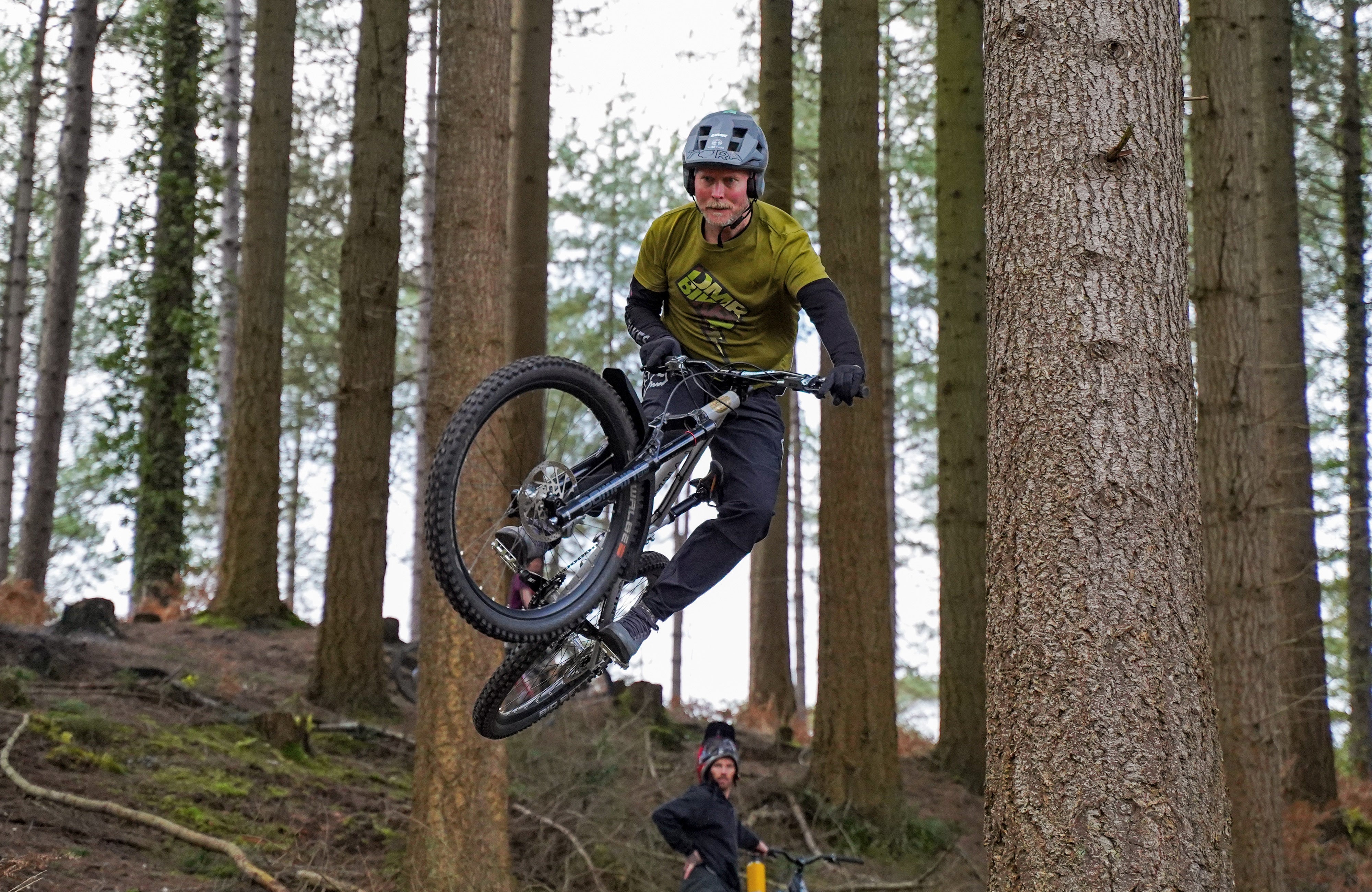 Team rider Steve Geall riding a bicycle, wearing a green t-shirt, with forest and trees in the background.