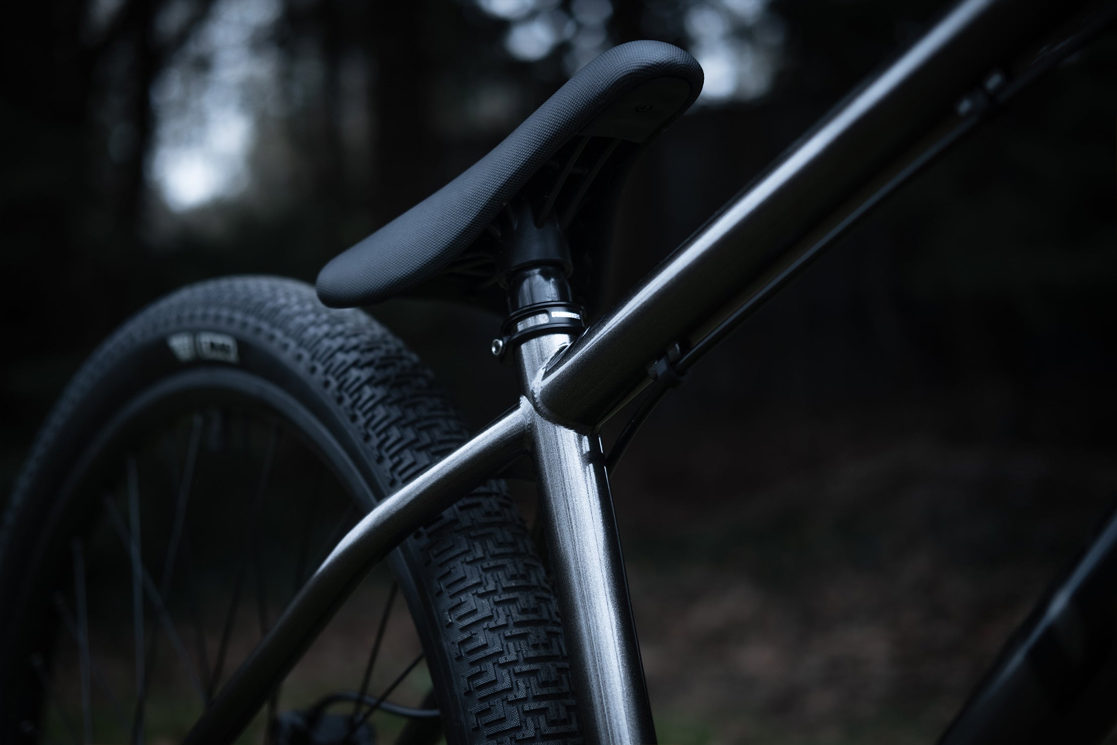 close-up of a dmr bikes sect custom dirt jumper frame bike in grey on grass with trees in the background