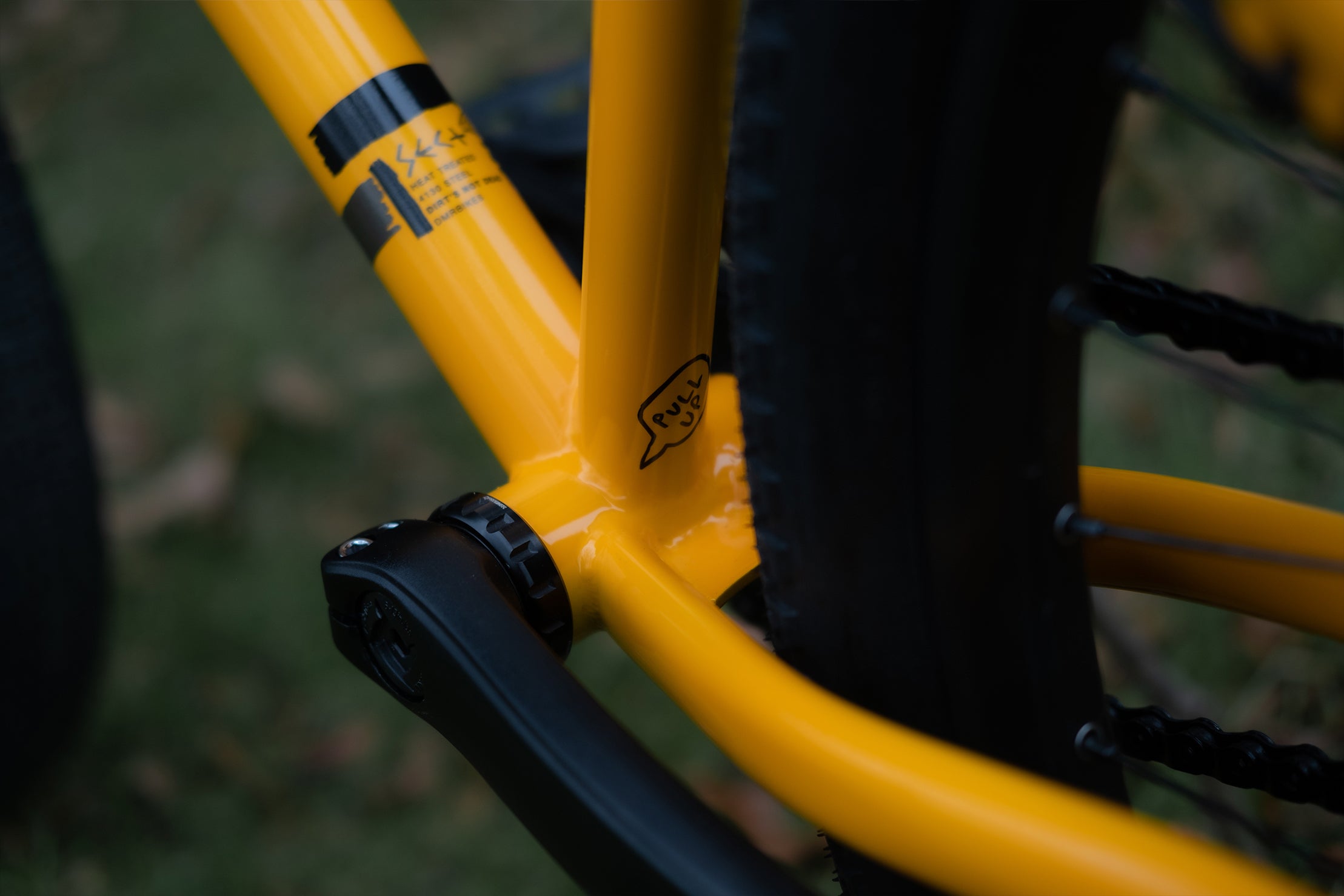 close-up of a dmr bikes sect custom dirt jumper frame bike in yellow on grass with trees in the background