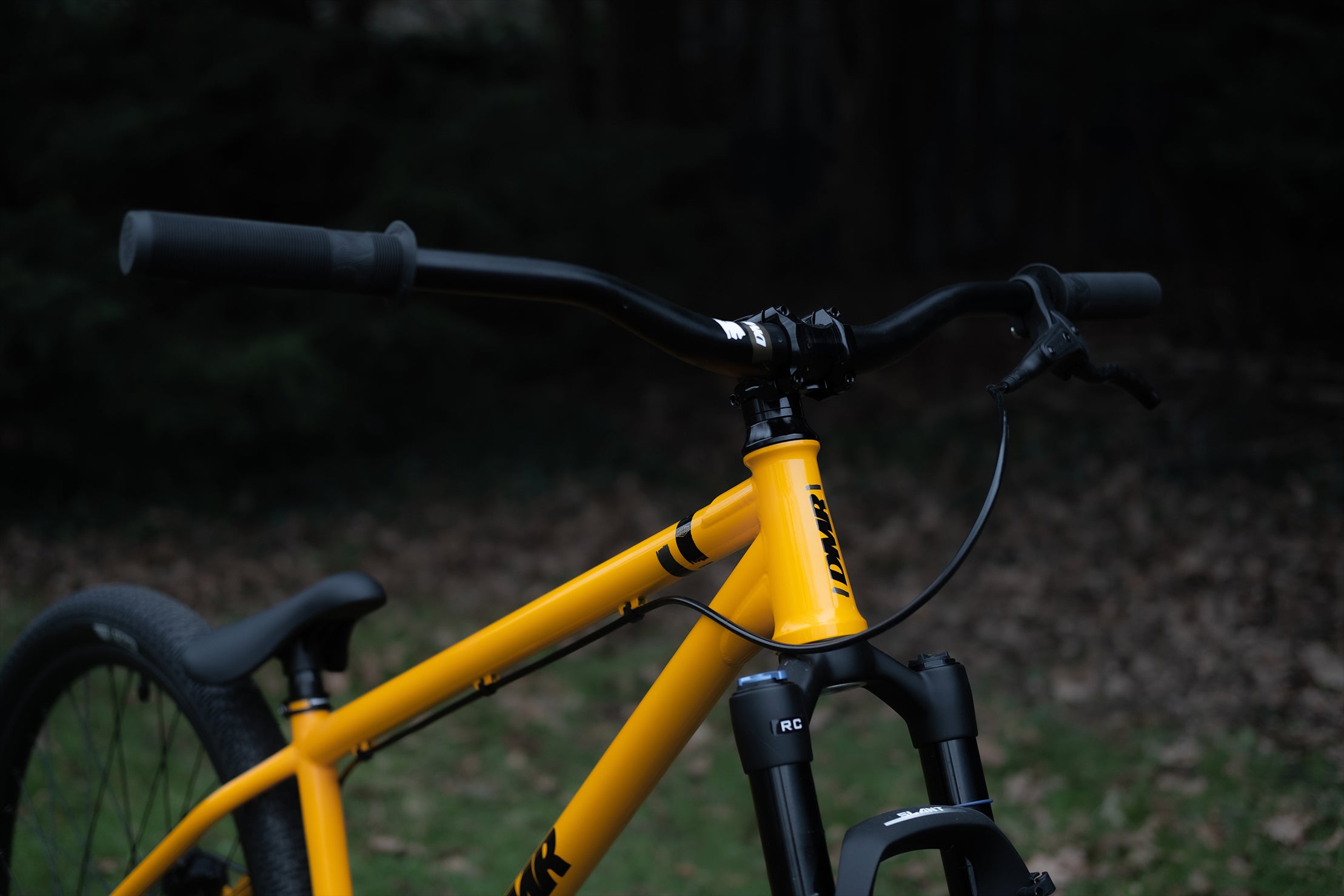 close-up of a dmr bikes sect custom dirt jumper frame bike in yellow on grass with trees in the background