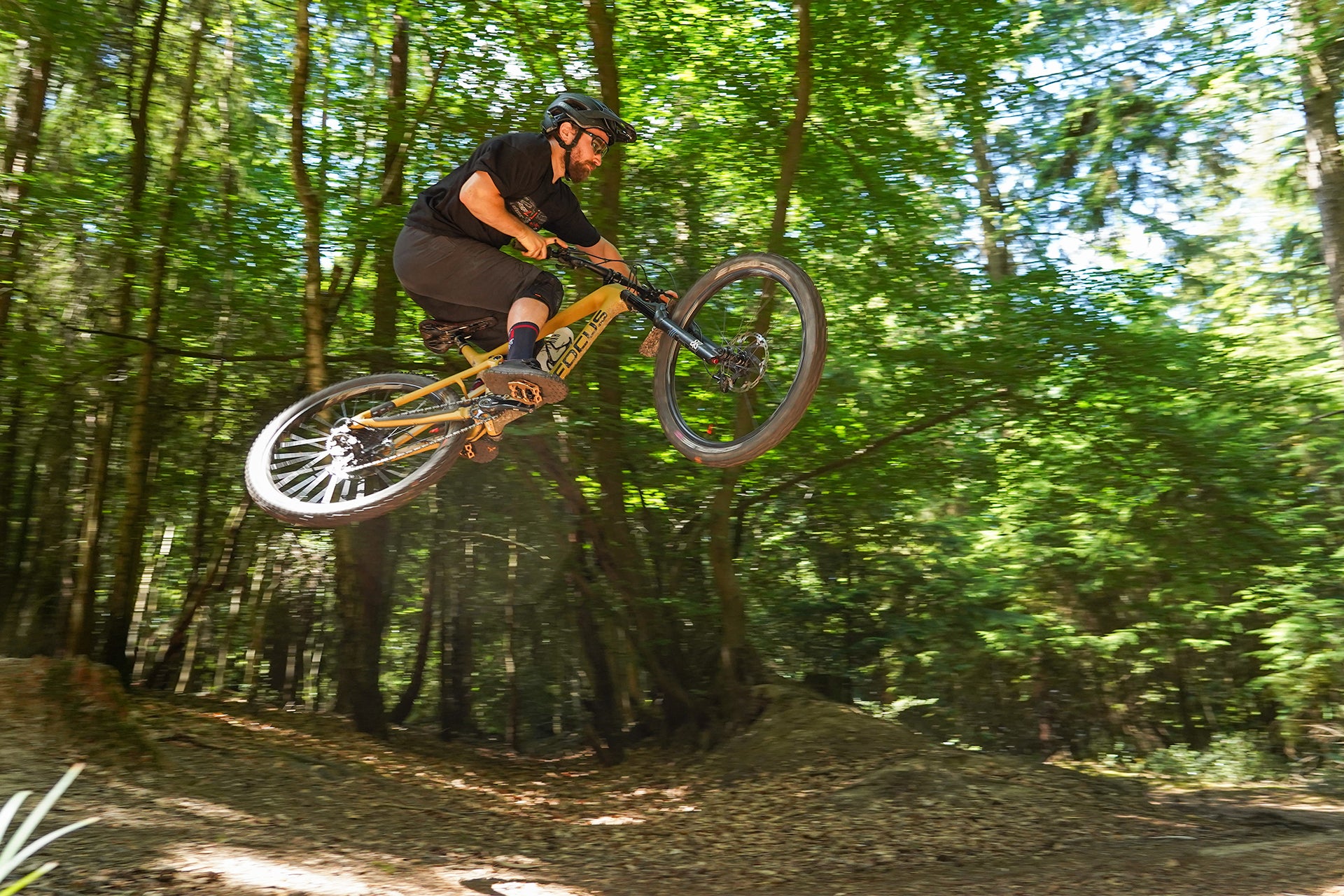 Light Bronze DMR VMAX clipless clip-in clip clipped SPD off-road mountain cycling bicycle bike pedalling pedal product, being used on an off-road mountain cycling cycle bicycle bike, pictured riding off a jump in the woods.